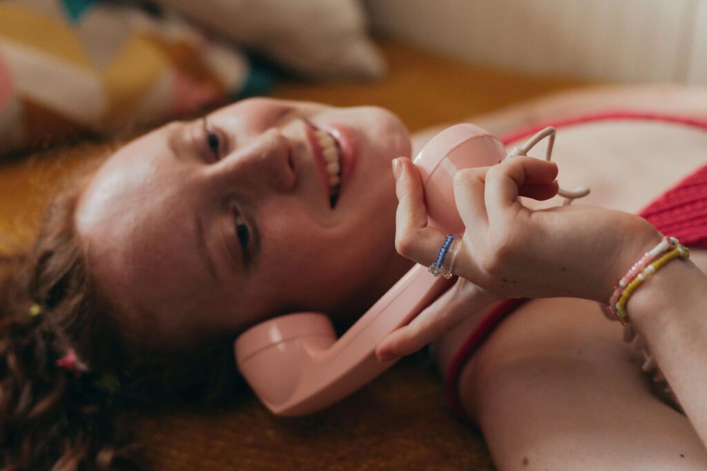 Mulher sorrindo ao falar em um telefone antigo rosa, ilustrando a nostalgia e a importância da comunicação para a intimidade no relacionamento.
