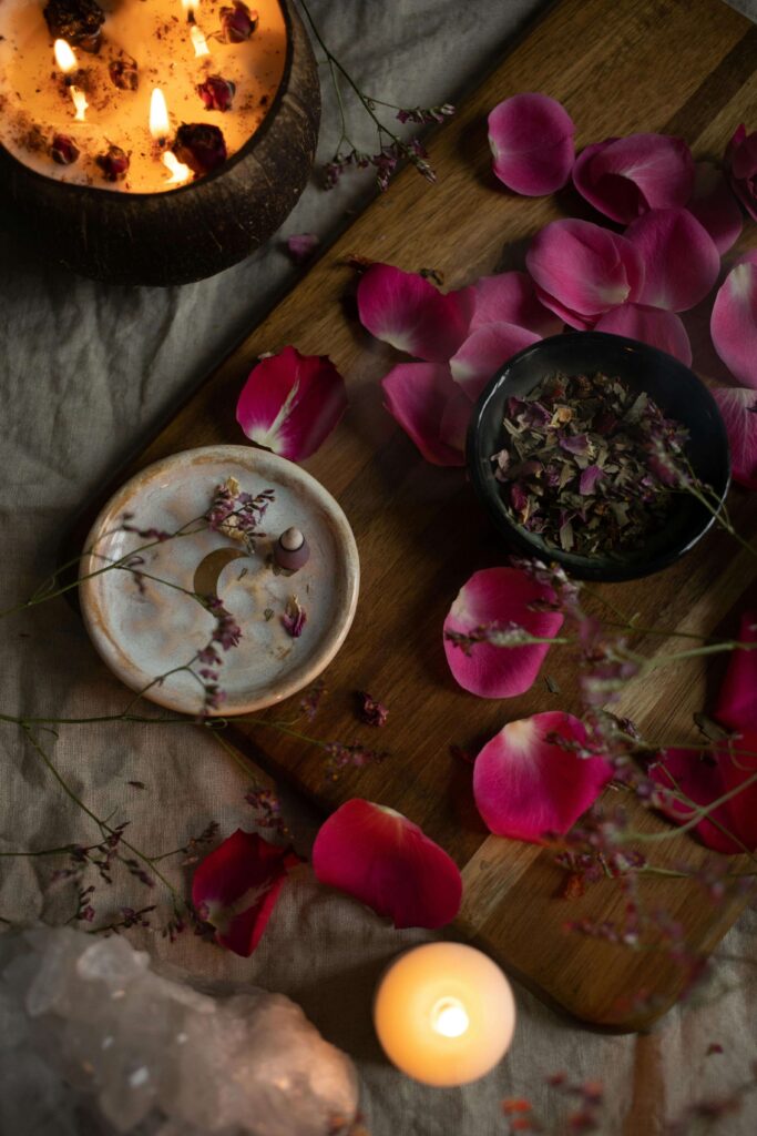 Cena aconchegante de um altar de bem-estar, com velas acesas em coco, pétalas de rosa espalhadas, incenso, ervas e um cristal, criando um ambiente sensorial e íntimo.