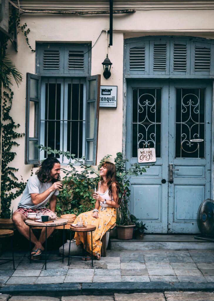 Casal conversando e sorrindo em um café ao ar livre, mostrando como sair da rotina e criar novas experiências fortalece a vida a dois.